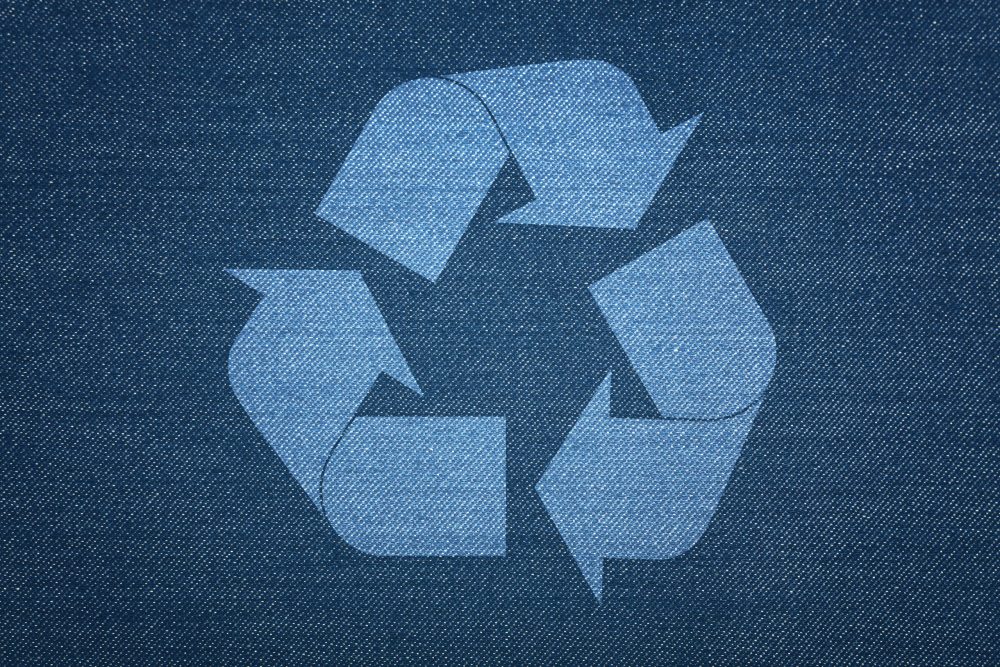 Dark indigo blue washed cotton jeans denim texture background with recycling logo icon