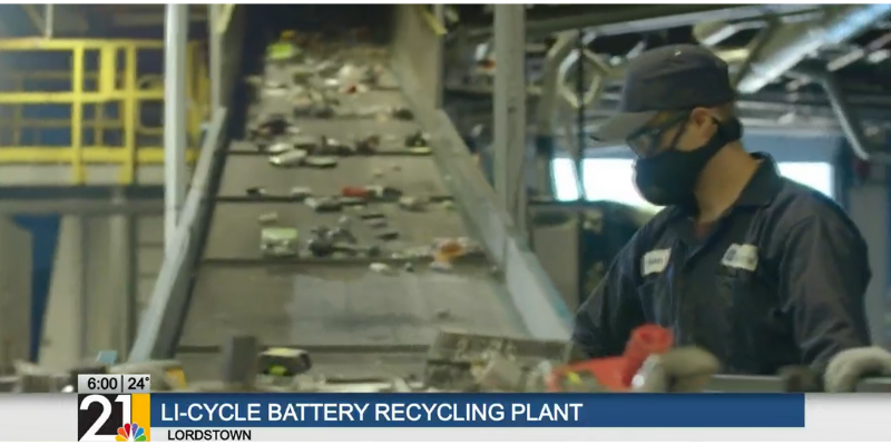 Screen capture of a broadcast showing Li-Cycle employee in safety gear sorting batteries at conveyor belt.