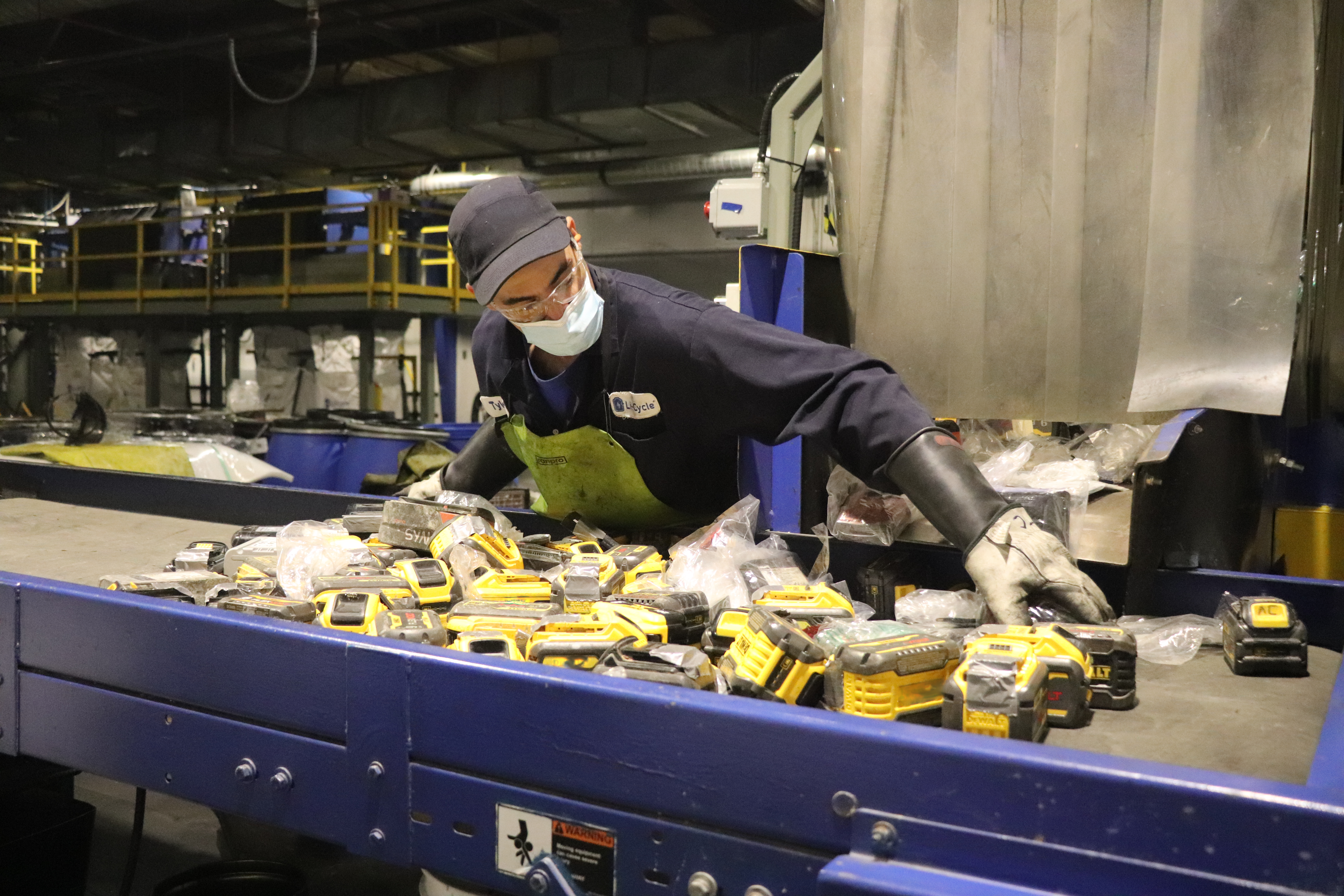 Li-Cycle employee wearing safety gear sorting assorted batteries.