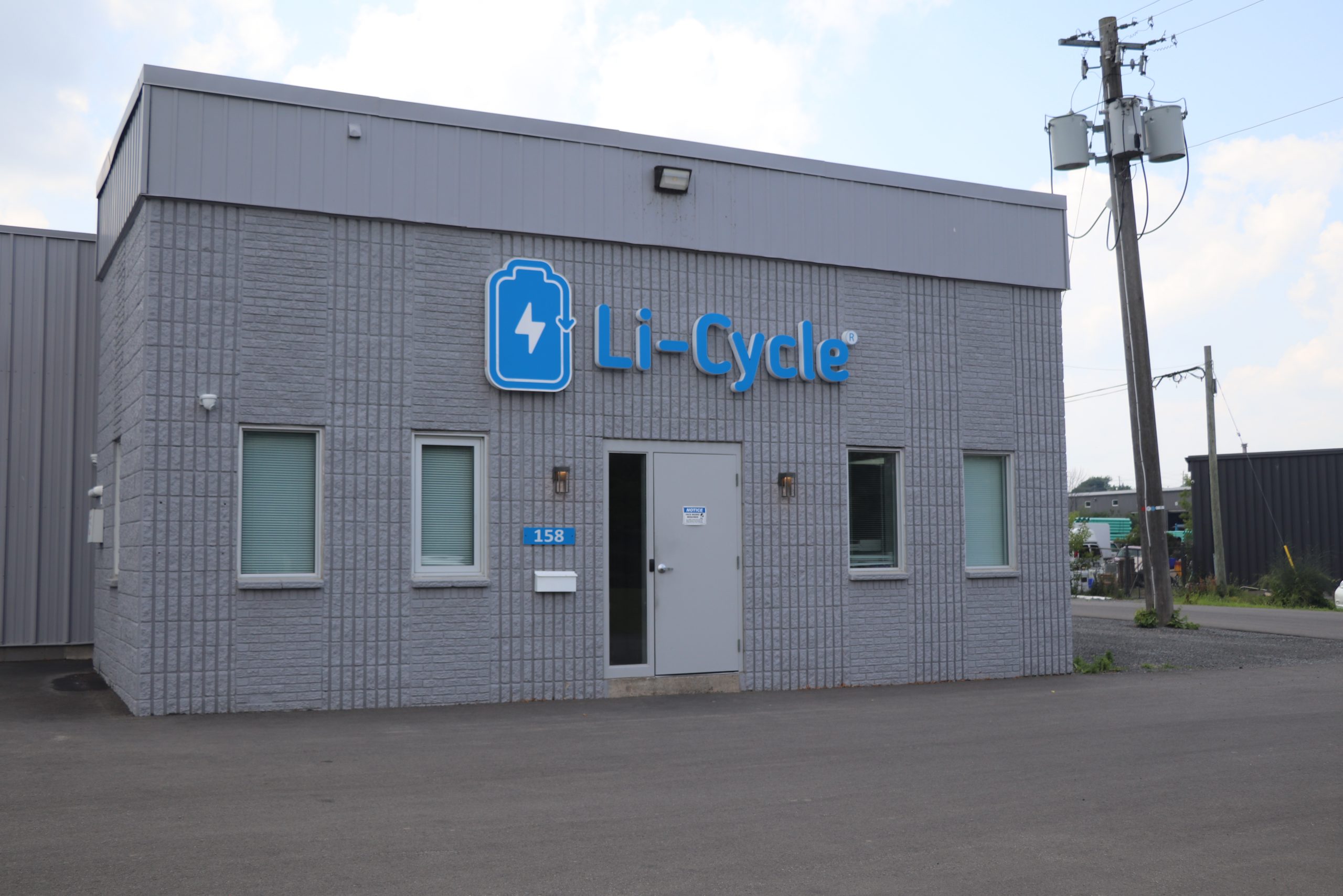 Photo of the exterior of a grey brick industrial building with a blue Li-Cycle logo above the entrance.