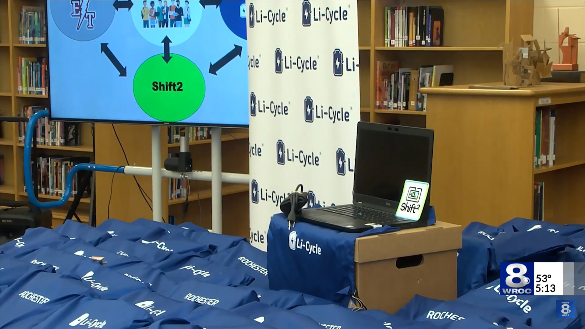 Screencapture from WROC news segment about Li-Cycle's donation of laptops to Edison Tech Highschool students. Photo shows a laptop with blue Li-Cycle branded tote bags.