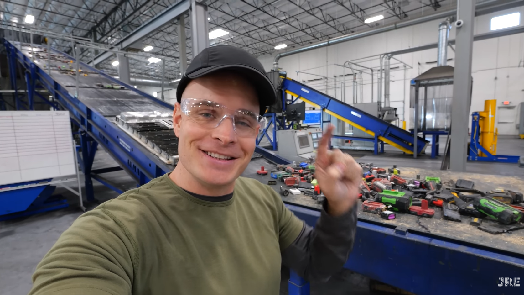 Man wearing safety goggles standing in front of conveyor belt wih various batteries on it.